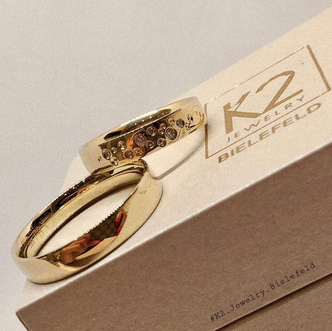 Goldene Eheringe mit Sternenhimmelbesatz auf einer K2 Jewelry Schatulle.