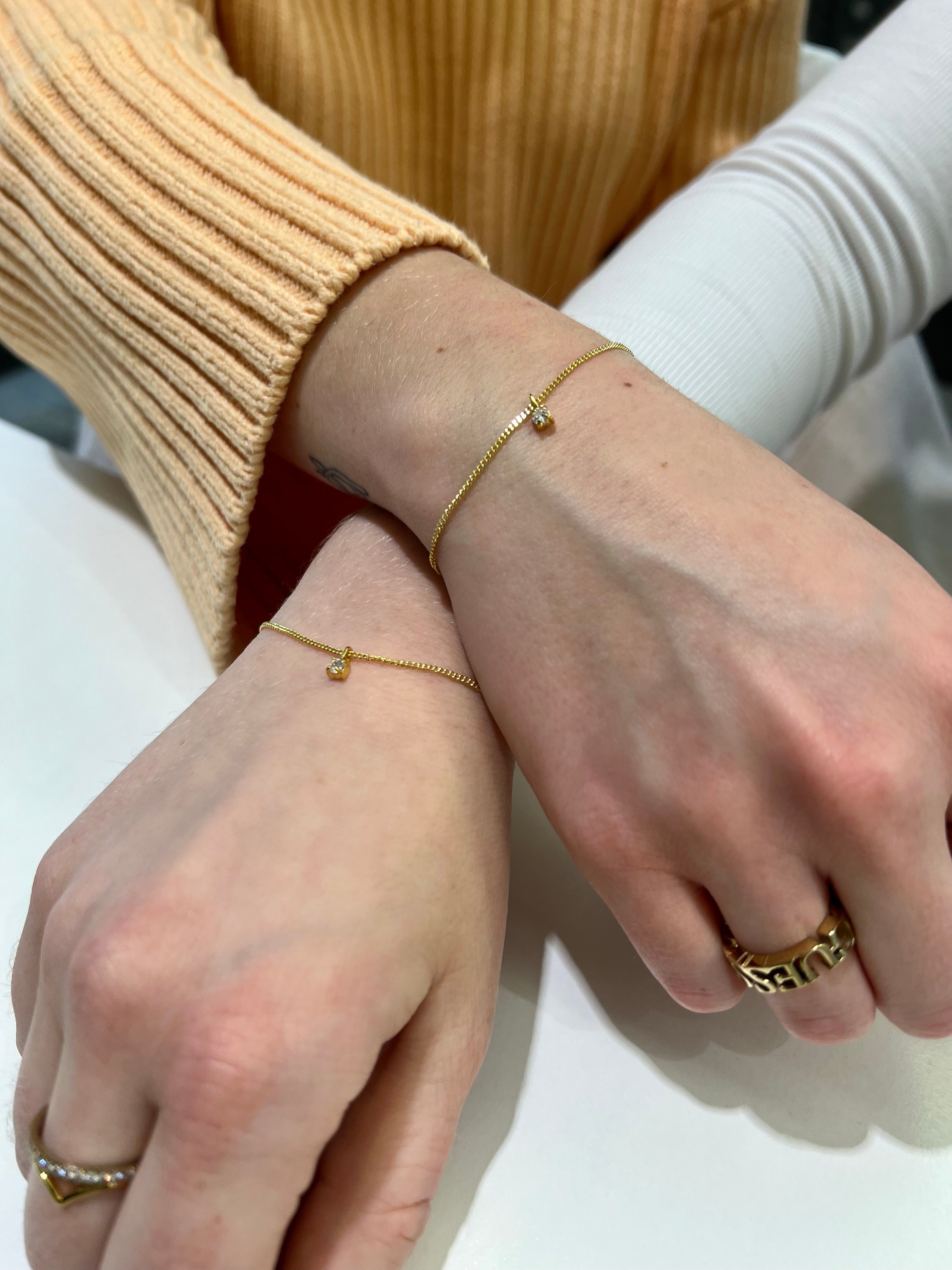 Zwei Freundinnen präsentieren ihre goldenen Permanent-Armbänder, die mit einem kleinen Anhänger geschmückt sind, in Bielefeld. 