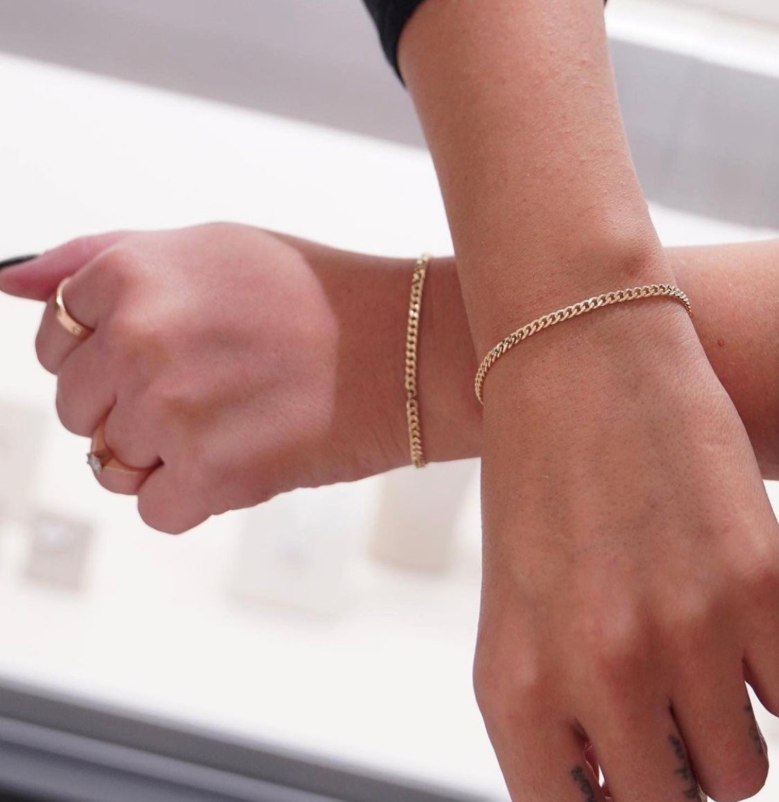 Zwei weibliche Hände kreuzen sich und präsentieren ihre goldenen Permanent Armbänder 